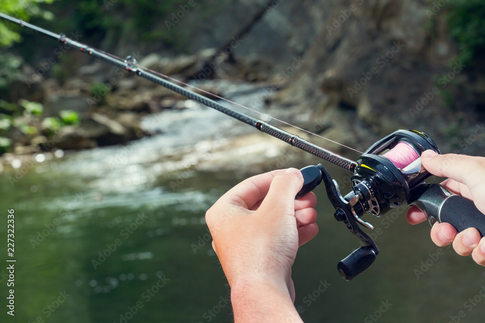 Fishing reel multiplier with a fishing rod in the hands of the fisherman.  Trout fishing in the river. Close up. Stock Photo
