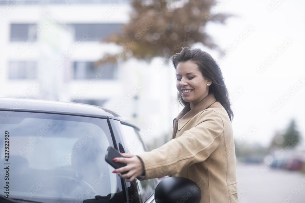 Junge Frau mit Smartphone checkt Carsharing Auto Junge Frau mit Smartphone checkt Carsharing Auto