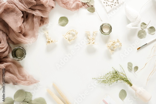 Creative home office desk workspace, festive composition with frame mock up, blanket, flowers, eucalyptus branches, love decor on white background. Pastel colors. Flat lay, top view.Copy space.
