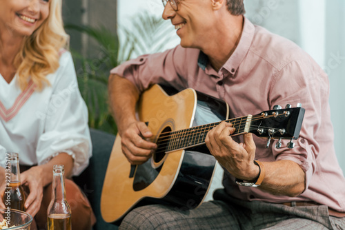 cropped shot of mature man playing guitar and looking at beautiful smiling woman at home