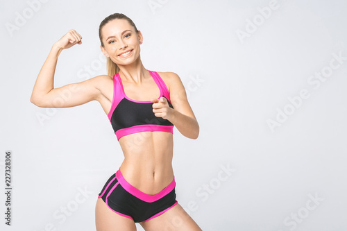 Fototapeta Naklejka Na Ścianę i Meble -  Cheerfully beautiful smiling sporty woman demonstrating biceps, isolated on white background.