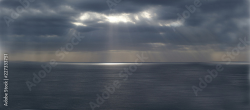 Meerespanorama mit Sonnenstrahlen durch dunkelen Himmel