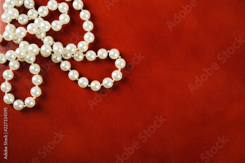 White pearl necklace on red leather background.