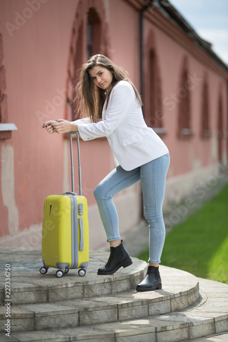 beautiful girl in a white jacket stands with a large yellow suitcase