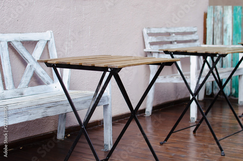 small wooden tables on metal legs and white benches of a street cafe. cozy coffee shop. colorful planks background