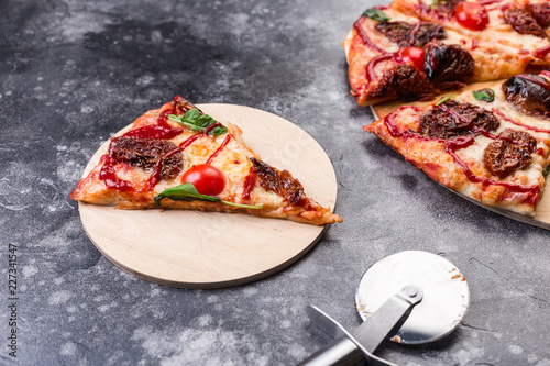 Pizza proshuto with sun-dried tomatoes, parmesan cheese on a wooden plate on grey table slice photo