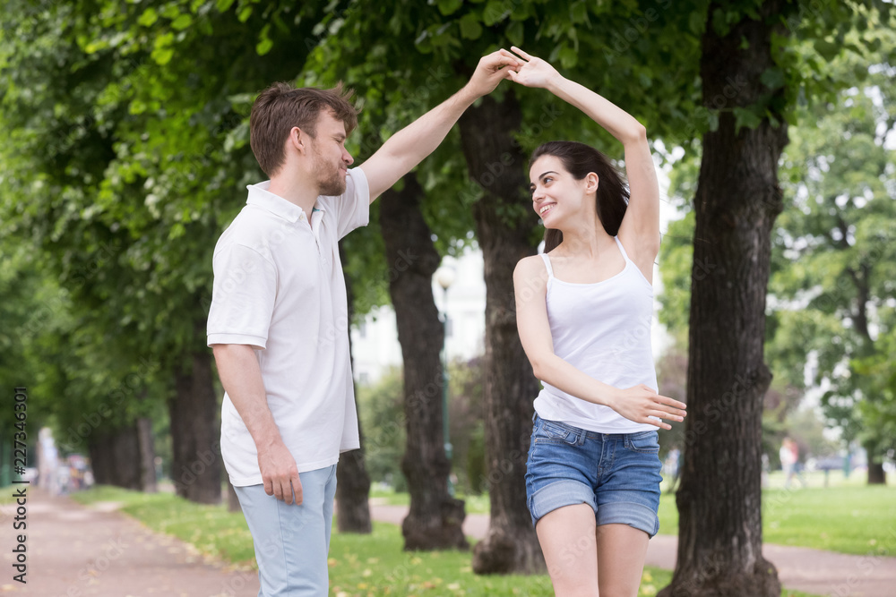 Young attractive couple in love wear casual summer clothes spend free time together in park. Happy girl and guy holding hands and dancing Romantic relations or friendship between man and woman concept Young attractive couple in love wear casual summer clothes spend free time together in park. Happy girl and guy holding hands and dancing Romantic relations or friendship between man and woman concept
