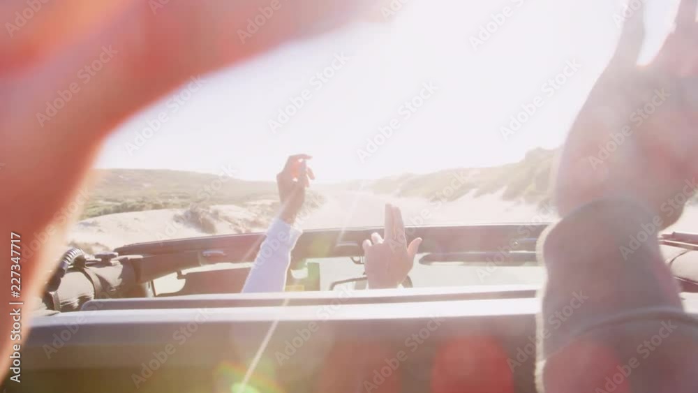 Male friends in open top car with hands in the air, backlit