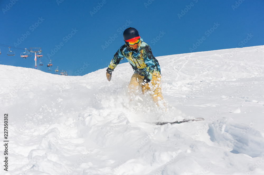 Professional active snowboarder in bright sportswear riding down a mountain slope