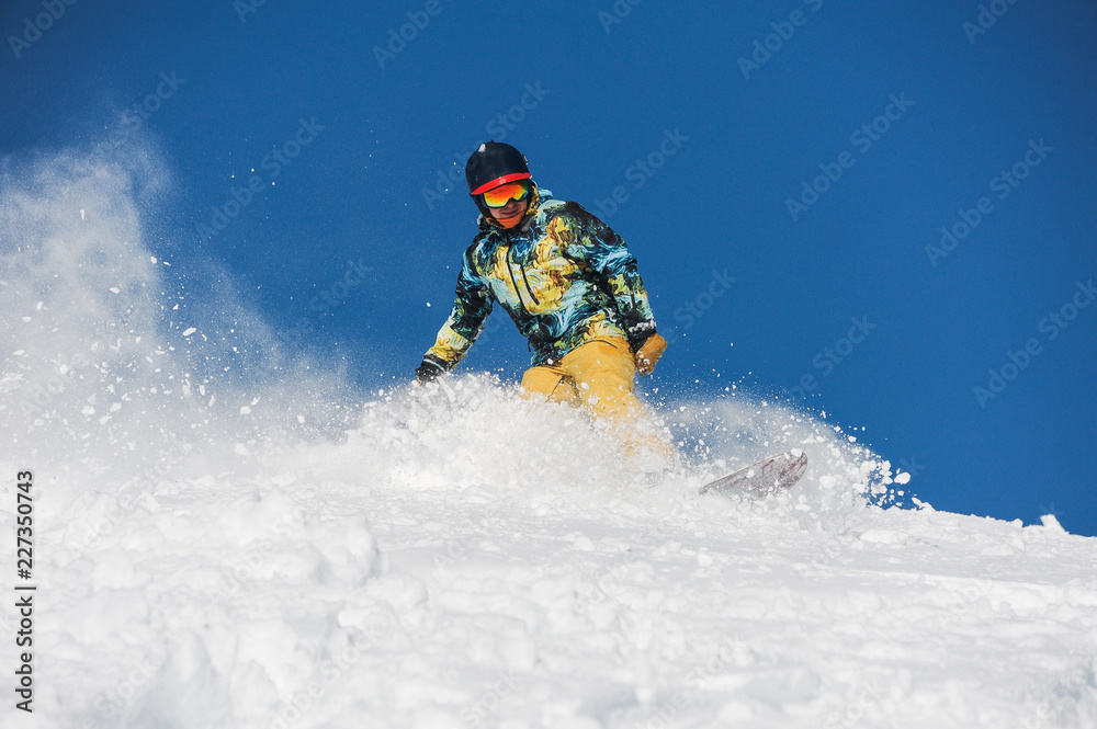 Snowboarder in bright sportswear riding down a powder mountain slope Snowboarder in bright sportswear riding down a powder mountain slope