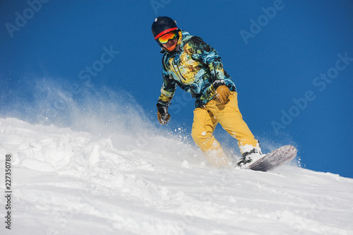 Active snowboarder in bright sportswear riding down a powder mountain slope