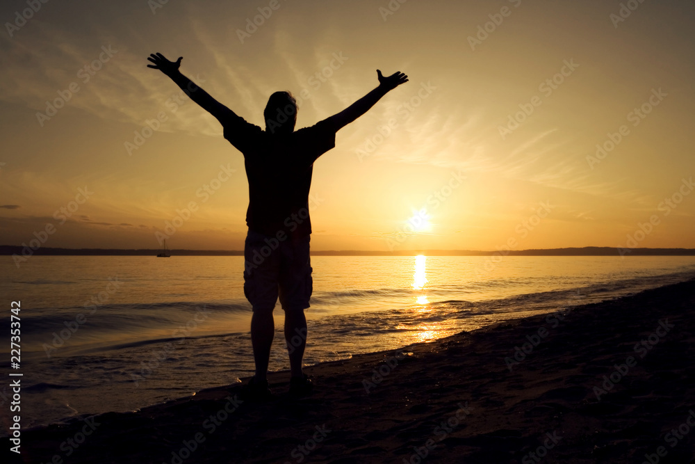 silhouette of man with open arms raised at sunset