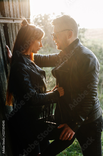 stylish couple in black clothes are looking at each other in a backlight against the background of an old wooden wall