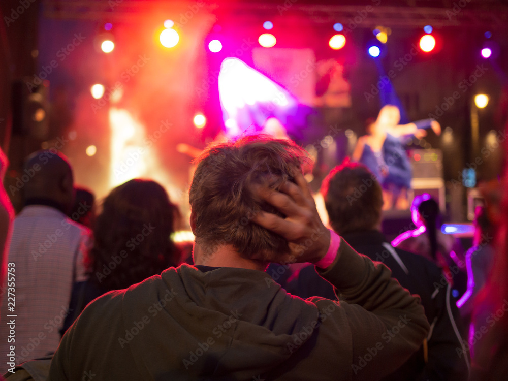Lonely sad young man in the crowd watching a concert, hand on head.