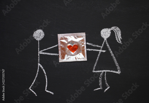 Chalk drawing man and woman holding together condom with red heart. Blackboard or chalkboard background. Safe sex or gentle love concept. Flat lay