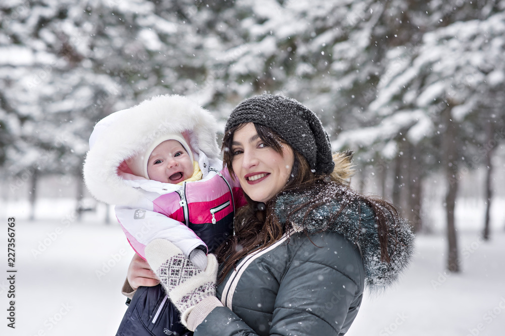 A young mother plays with a baby on the street during a snowfall