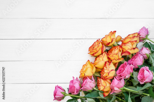 Pink and yellow roses on white wooden background. Copy space, top view. Greeting card.