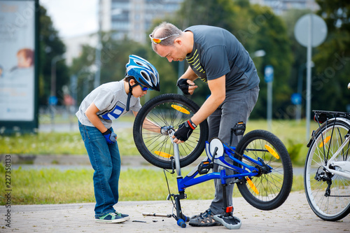 Cute little boy with his father repairing bicycle outdoors