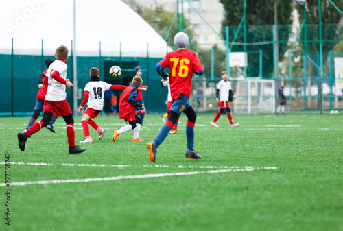 football teams - boys in red, blue, white uniform play soccer on the green field. boys dribbling. dribbling skills. Team game, training, active lifestyle, hobby, sport for kids concept © Natali
