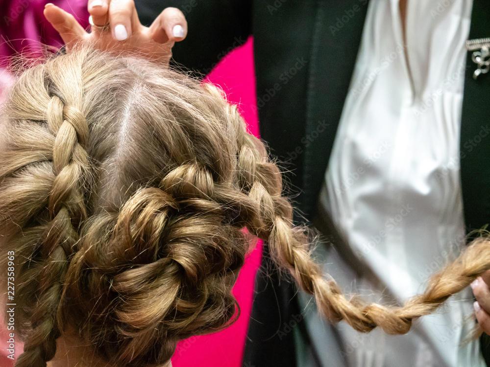 Fototapeta premium Hairdresser. Creating hair. Braiding pigtails. Blonde girl with pigtails.