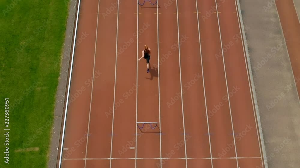 Female athletic jumping over hurdle on sports track 4k