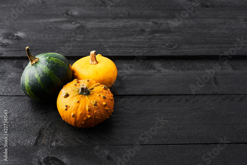 Simple autumn background with yellow, orange and green pumpkins on black wood with copy space. Top view.