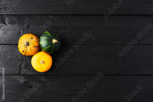 Simple autumn background with yellow, orange and green pumpkins on black wood with copy space. Top view.
