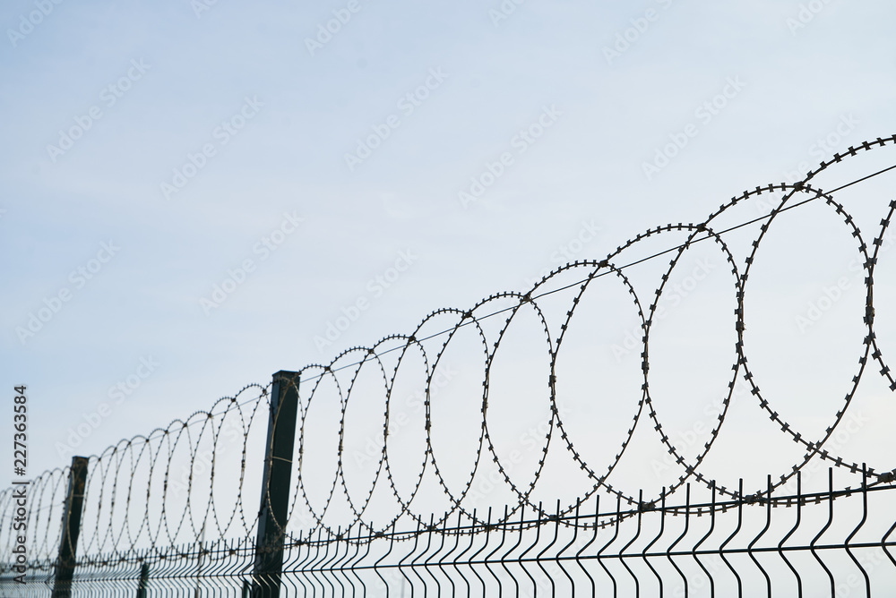 Barbed wire against cloudy sky, close-up. Metal fence with barbed wire, outdoors Barbed wire against cloudy sky, close-up. Metal fence with barbed wire, outdoors