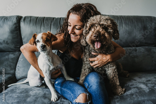 Photography Young beautiful woman playing with her dogs in her sofa at home