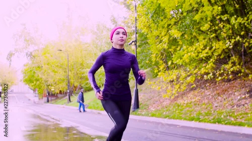 Dolly shot, slow motion. Young woman running in the park at autumn day