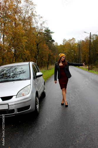 the autumn day the car broke down and the girl in a dress with a hat catches another car to help