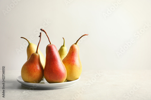 Plate with ripe pears on light background. Space for text