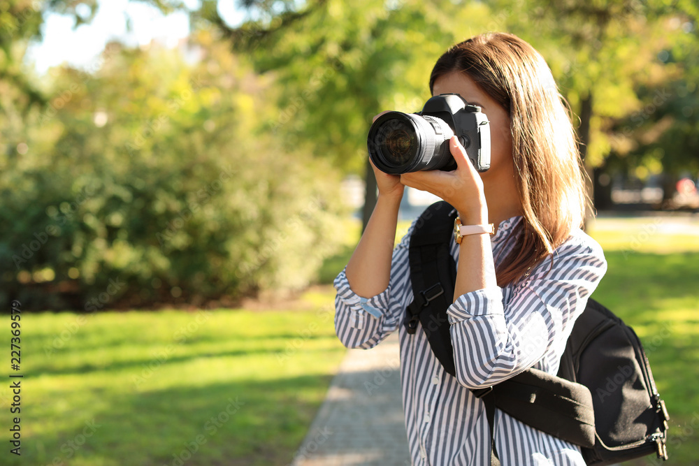 Young female photographer taking photo with professional camera in park. Space for text