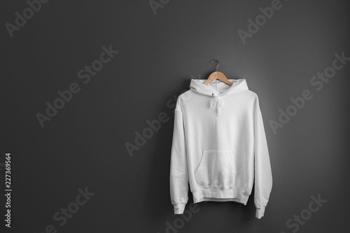 New hoodie sweater with hanger on grey wall. Mockup for design