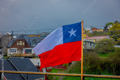 Outdoor view of Chilean flag waving with beautiful and colorful houses on stilts palafitos behind in the horizont in Castro, Chiloe Island photo