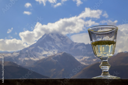 Бокал вина стоит на деревянных перилах на фоне горы.Горизонтально.