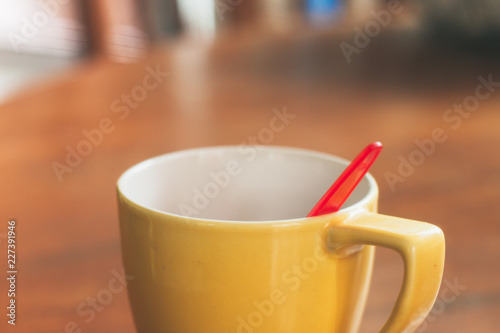 Yellow cup with red spoon on the table.