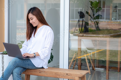 Closeup image of an asian woman using and typing on laptop keyboard while sitting outdoor