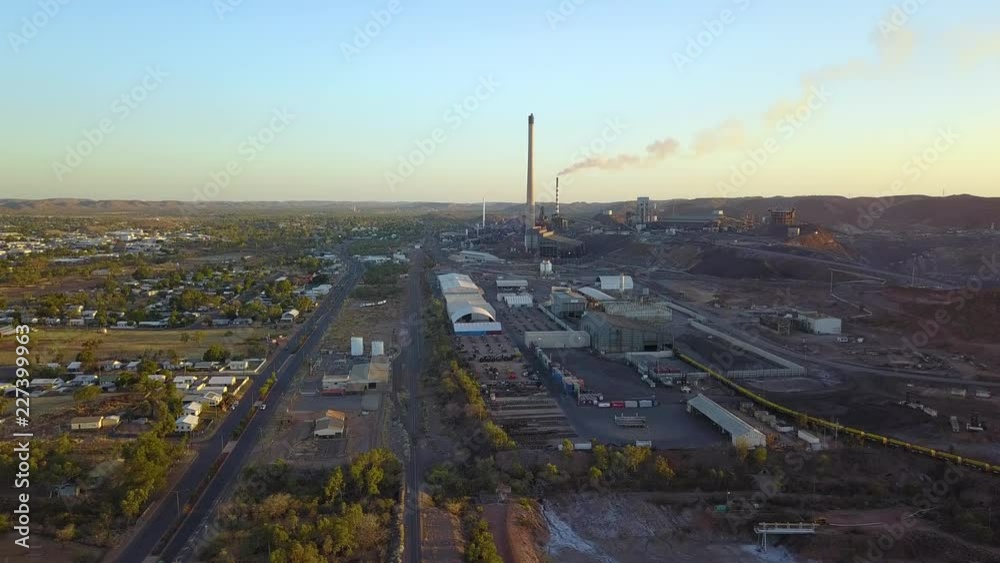 Vertically rising drone footage of large mining complex with two large smoke stacks, one of which has smoke coming out. Locationg Mt Isa, Queensland, Australia.
