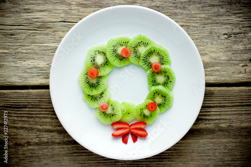 Funny xmas food idea for kids - kiwi strawberry edible Christmas wreath on a white plate