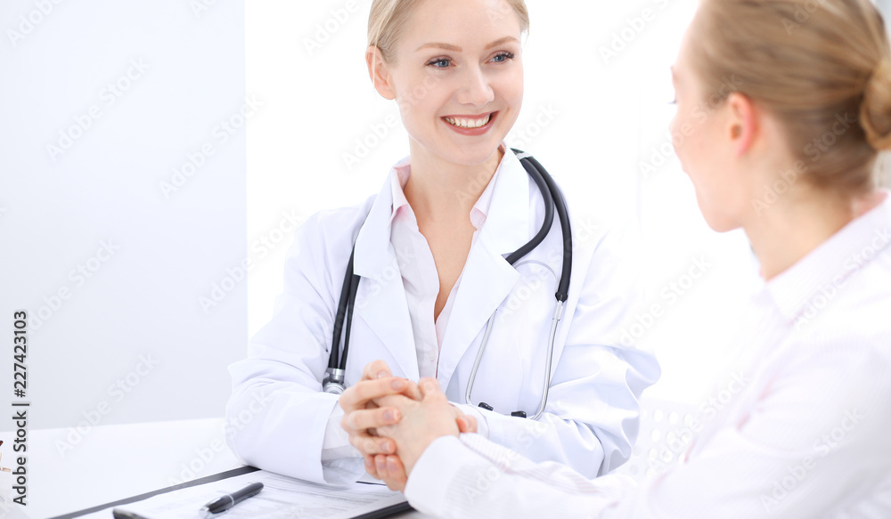 Blonde female doctor and patient talking in hospital office. Health care and client service in medicine Blonde female doctor and patient talking in hospital office. Health care and client service in medicine