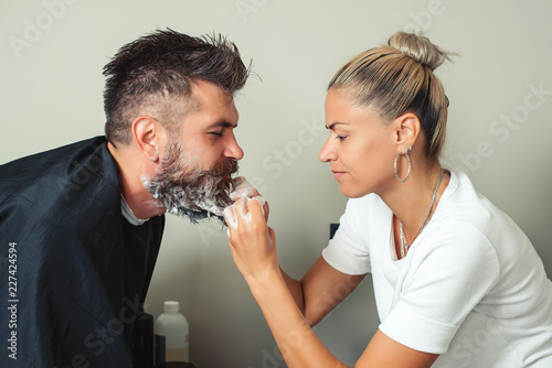 Barber paints beard and mustache in black color of hipster man in barbershop. Hairstylist hairdresser washing customer beard - man relaxing in hairdressing beauty salon. Cleaning beard Barbershop.