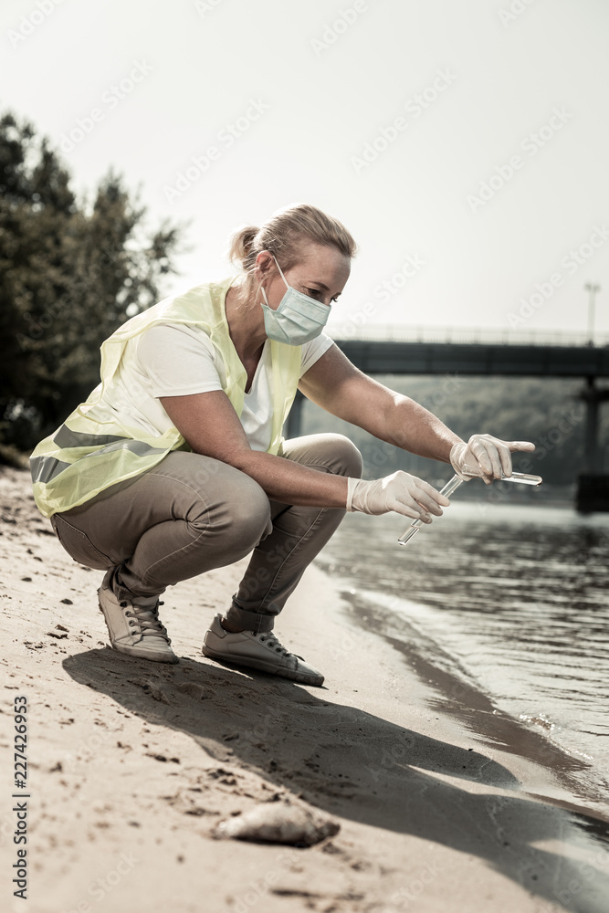 Inspector and river. Blonde-haired sanitary inspector wearing beige trousers and yellow vest working near the river