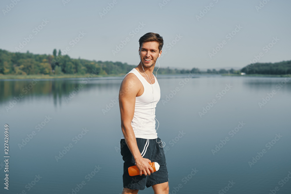 Portrait of smiling and relaxing athletic man holding bottle of