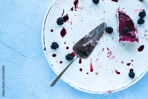 Brombeer-cheesecake Käsekuchen letzte Stück auf weißem Teller mit Tortenheber auf hellem Untergrund mit negativem Raum für Text von oben bei tageslicht fotografiert
