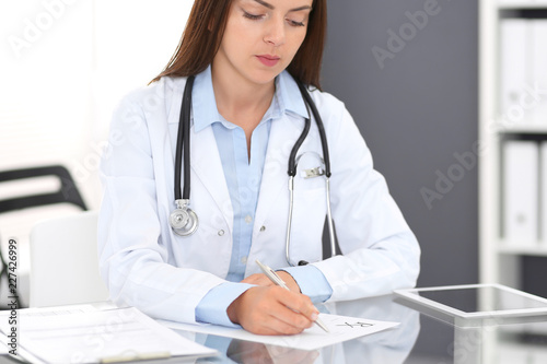 Doctor woman at work. Portrait of female physician filling up medical prescription form while sitting the glass desk at clinic or hospital. Medicine and healthcare concept