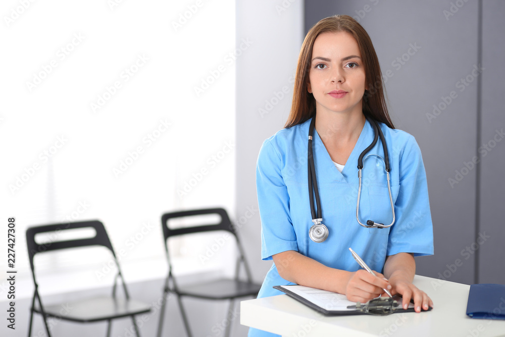 Doctor woman at work. Portrait of female physician filling up medical form while standing near reception desk at clinic or emergency hospital. Medicine and healthcare concept Doctor woman at work. Portrait of female physician filling up medical form while standing near reception desk at clinic or emergency hospital. Medicine and healthcare concept