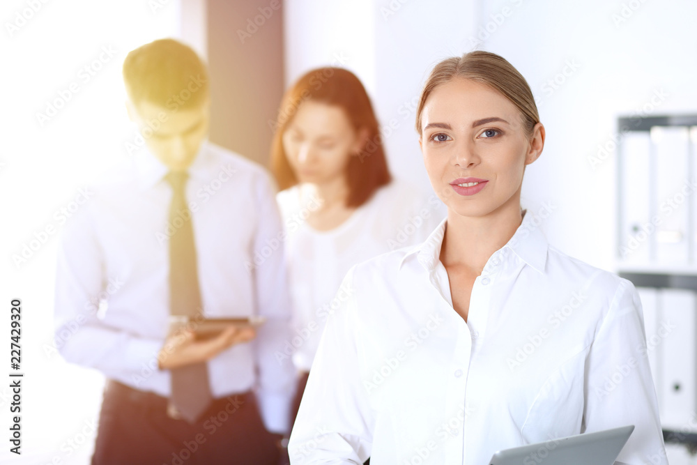 Beautiful blonde businesswoman standing straight in a brightly lit office at the background of colleagues or partners. Business concept Beautiful blonde businesswoman standing straight in a brightly lit office at the background of colleagues or partners. Business concept