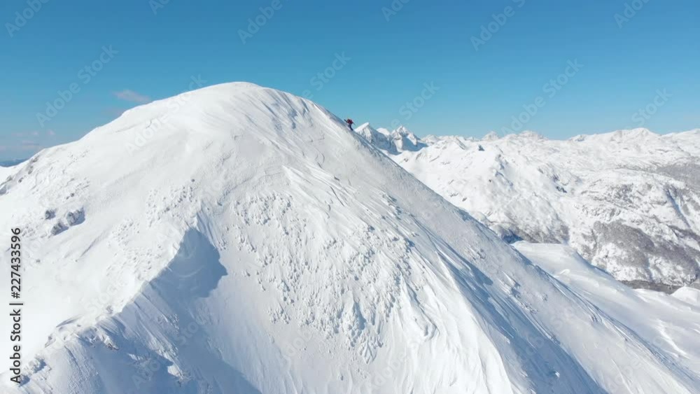 Aerial unrecognizable skier hiking up the snowy mountain in sunny winter