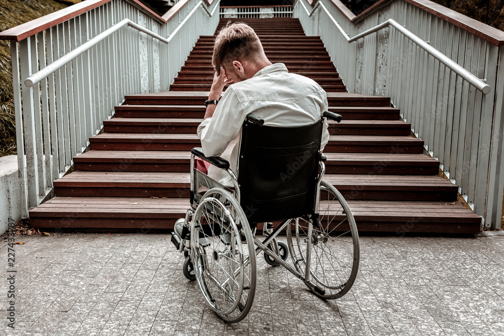Many stairs. Horizontal image of depressed disabled man sitting in the